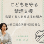 本目さよ台東区議会議員が「こどもを守る禁煙支援」について発信する告知画像。 背景は淡いベージュとレインボーラインのデザインで、 中央に「こどもを守る禁煙支援　希望する人を支える仕組み」と大きく記載。 左下に考える表情の本目さよ議員、右下に禁煙マークのイラストが配置されている。